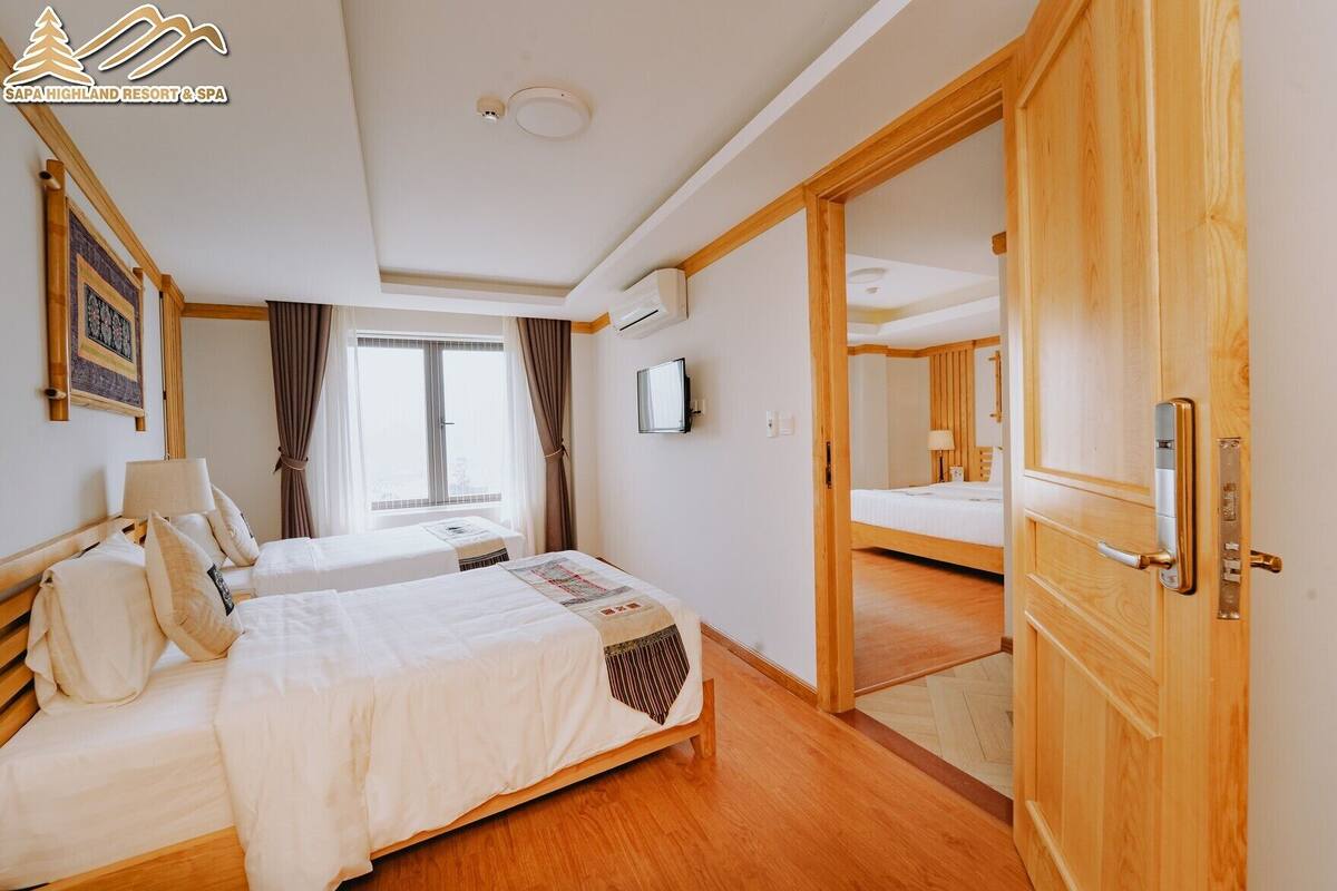 Ein Hotelzimmer mit zwei Betten, einem Fernseher, einem Fenster mit Vorhängen und einer Holztür.
