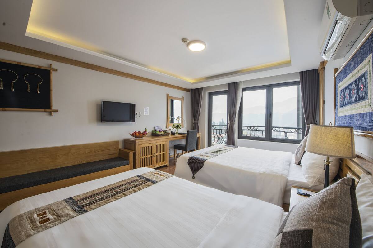Ein Hotelzimmer mit zwei Betten, einem Schreibtisch, einem Fernseher und einem Balkon mit Blick.