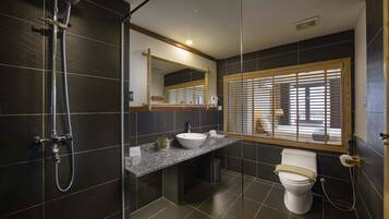 A modern bathroom with a glass-enclosed shower, a granite countertop sink, a toilet, and a window with wooden blinds.