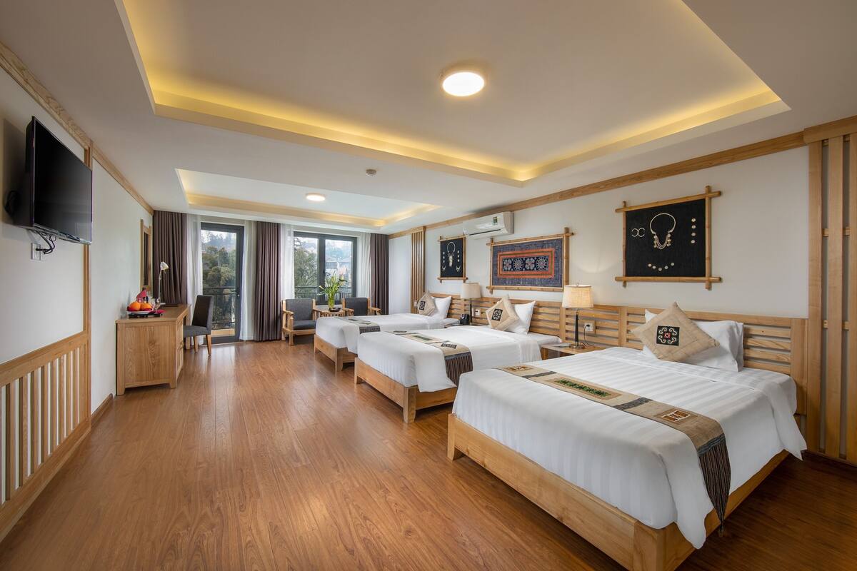 Ein Hotelzimmer mit vier Betten, einem Fernseher, einem Schreibtisch und Blick ins Freie.