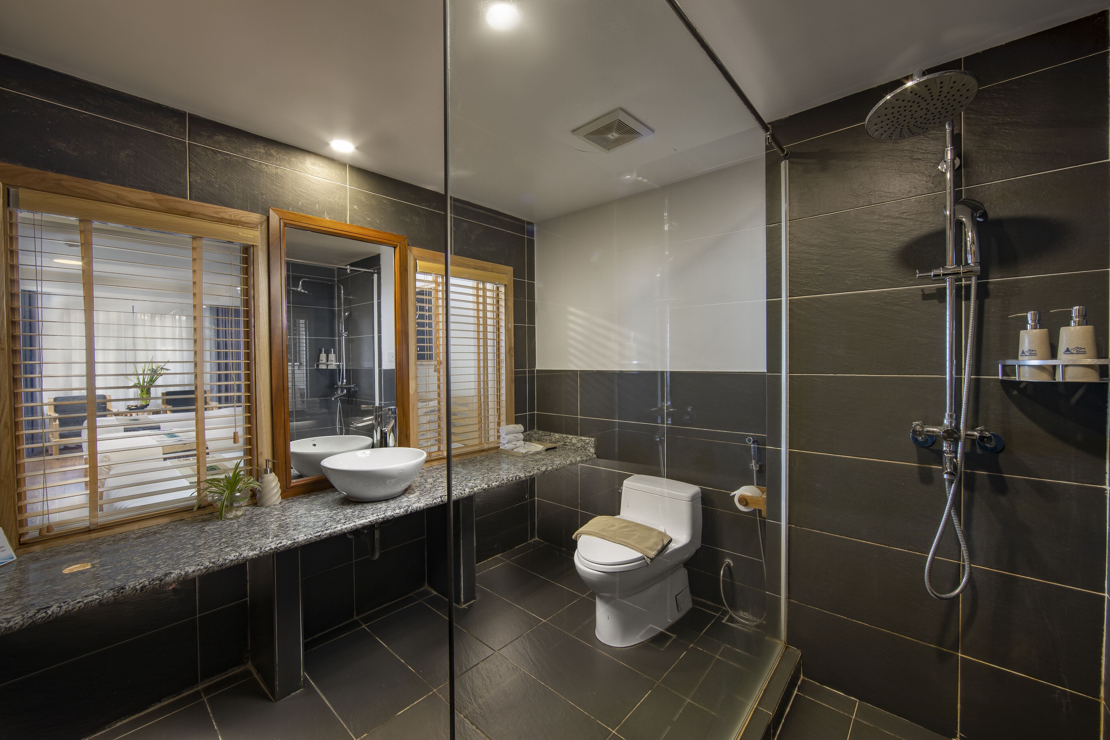 A modern bathroom with a large mirror, two sinks, a toilet, and a shower.