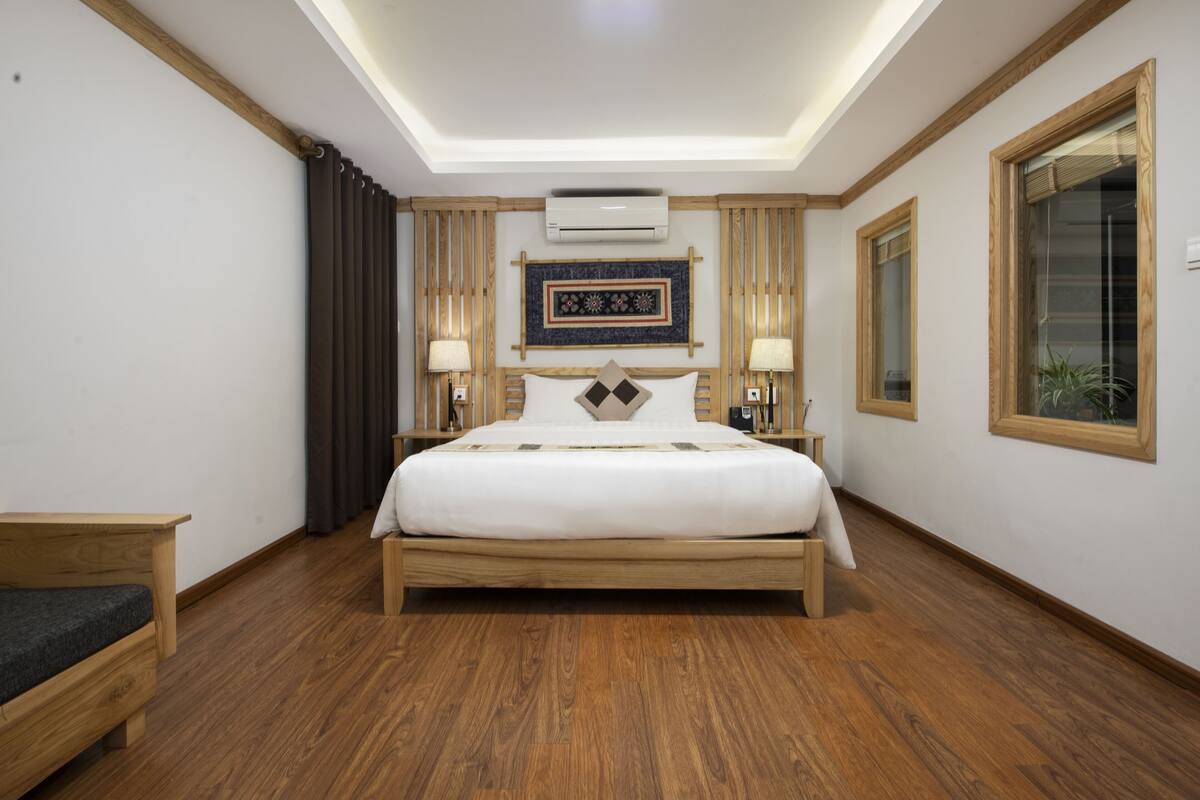 Ein Hotelzimmer mit einem hölzernen Bett, einem Nachttisch, einer Lampe und einem Fenster mit Blick.
