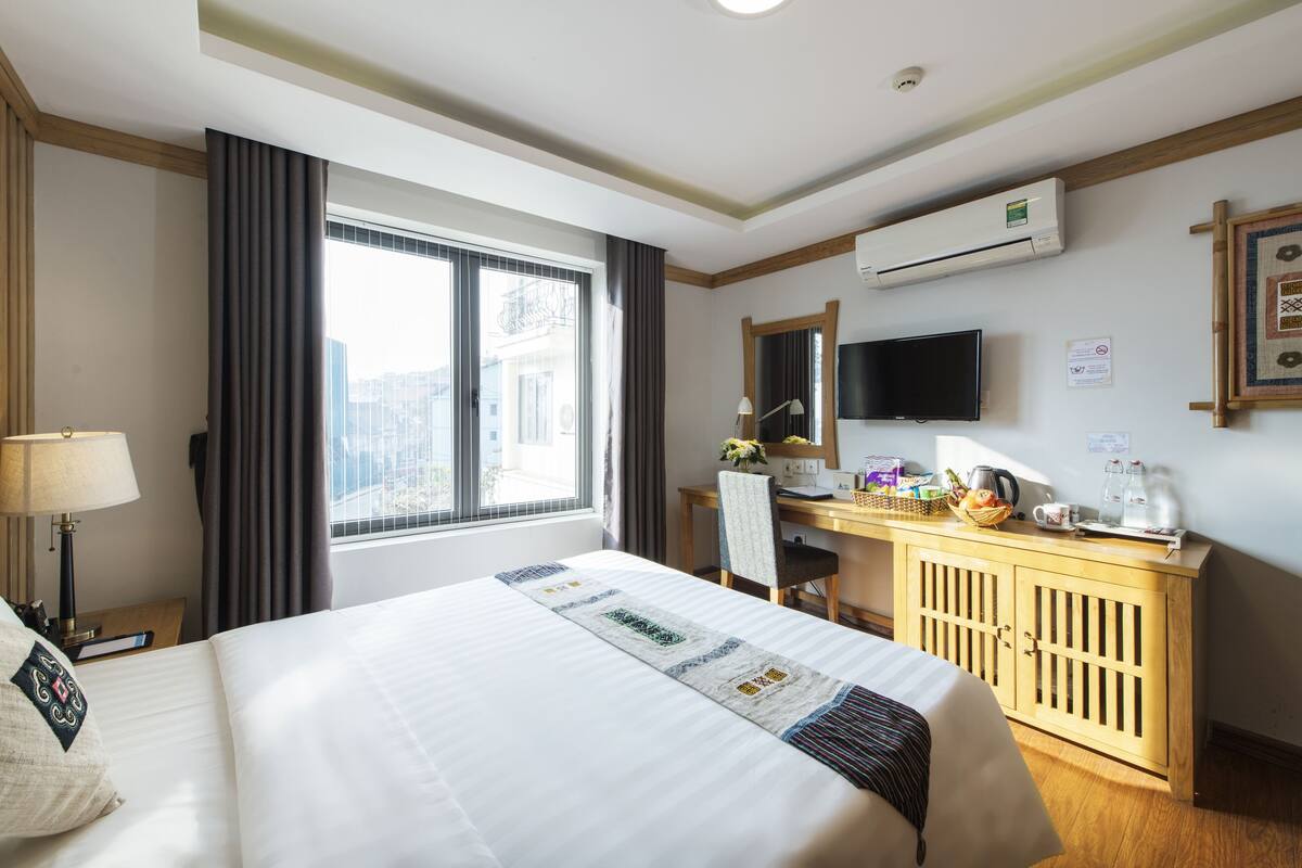 Ein Hotelzimmer mit einem großen Bett, einem Schreibtisch mit Computer, einem Fernseher und einer Klimaanlage.