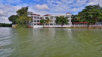 A multi-story waterfront hotel with balconies, surrounded by trees and a body of water.