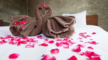 Relax in a serene bedroom with a plush bed, complete with a swan-shaped towel and rose petals.
