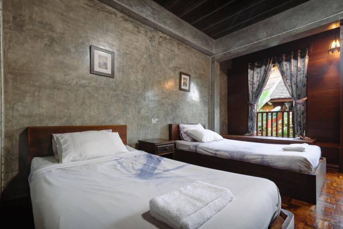 A room with two beds, a wooden ceiling, and a window with curtains.