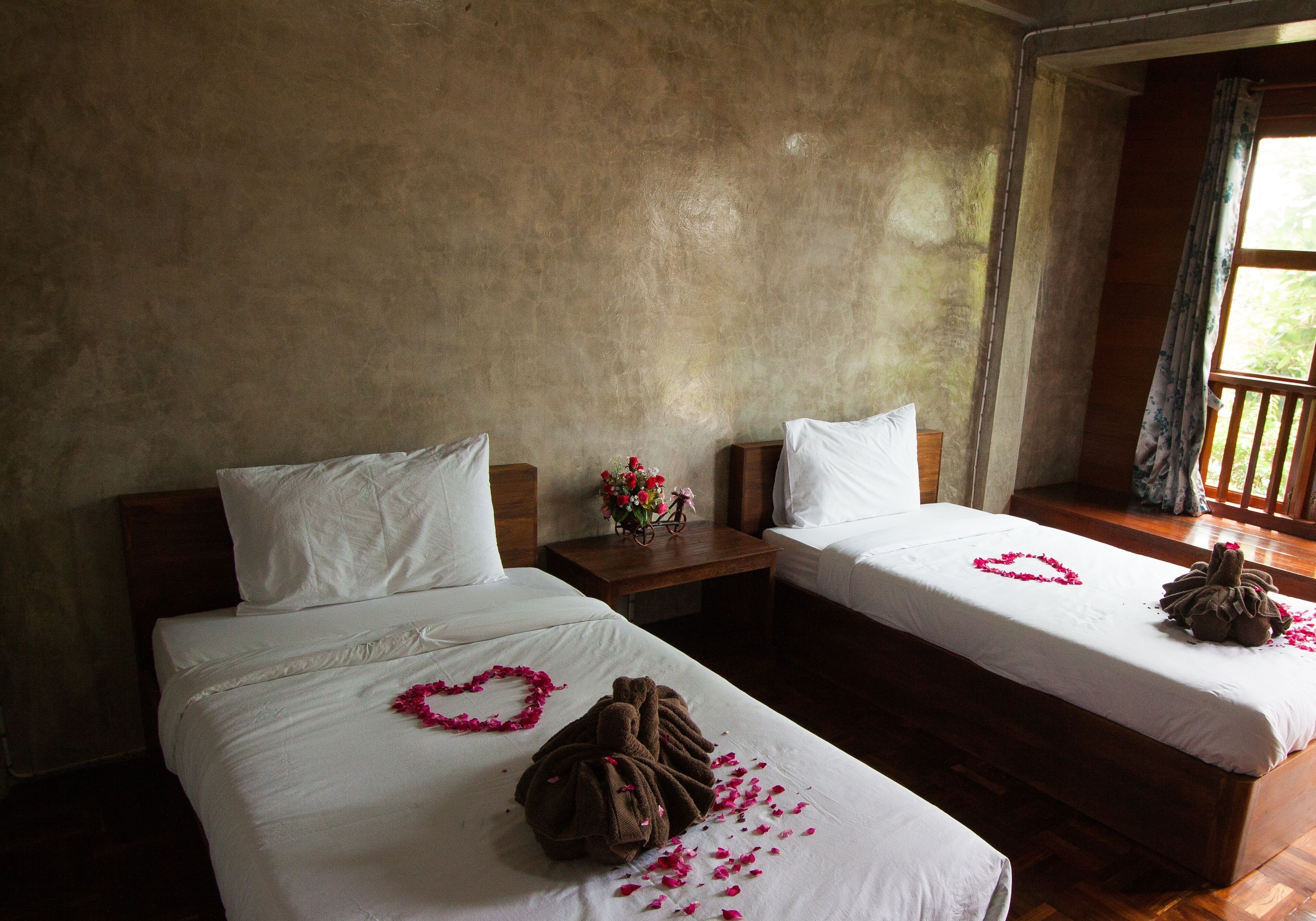 Two single beds with white linens, heart-shaped flower petals, and a brown towel on one bed.