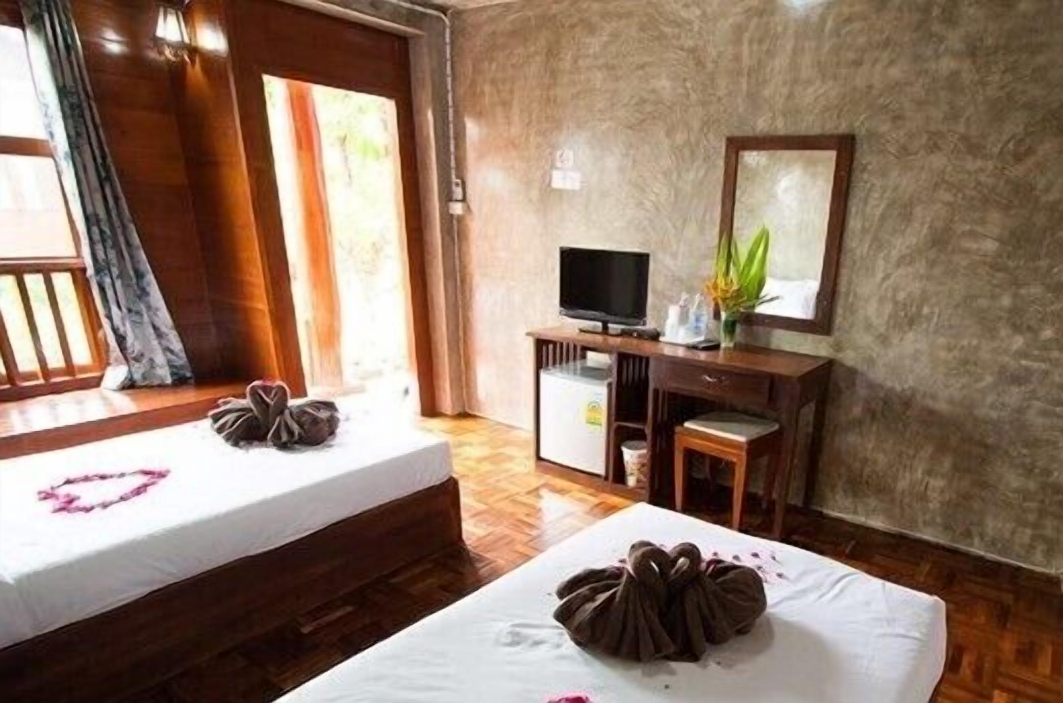A hotel room with two beds, a desk with a television, a mirror, and a small plant.