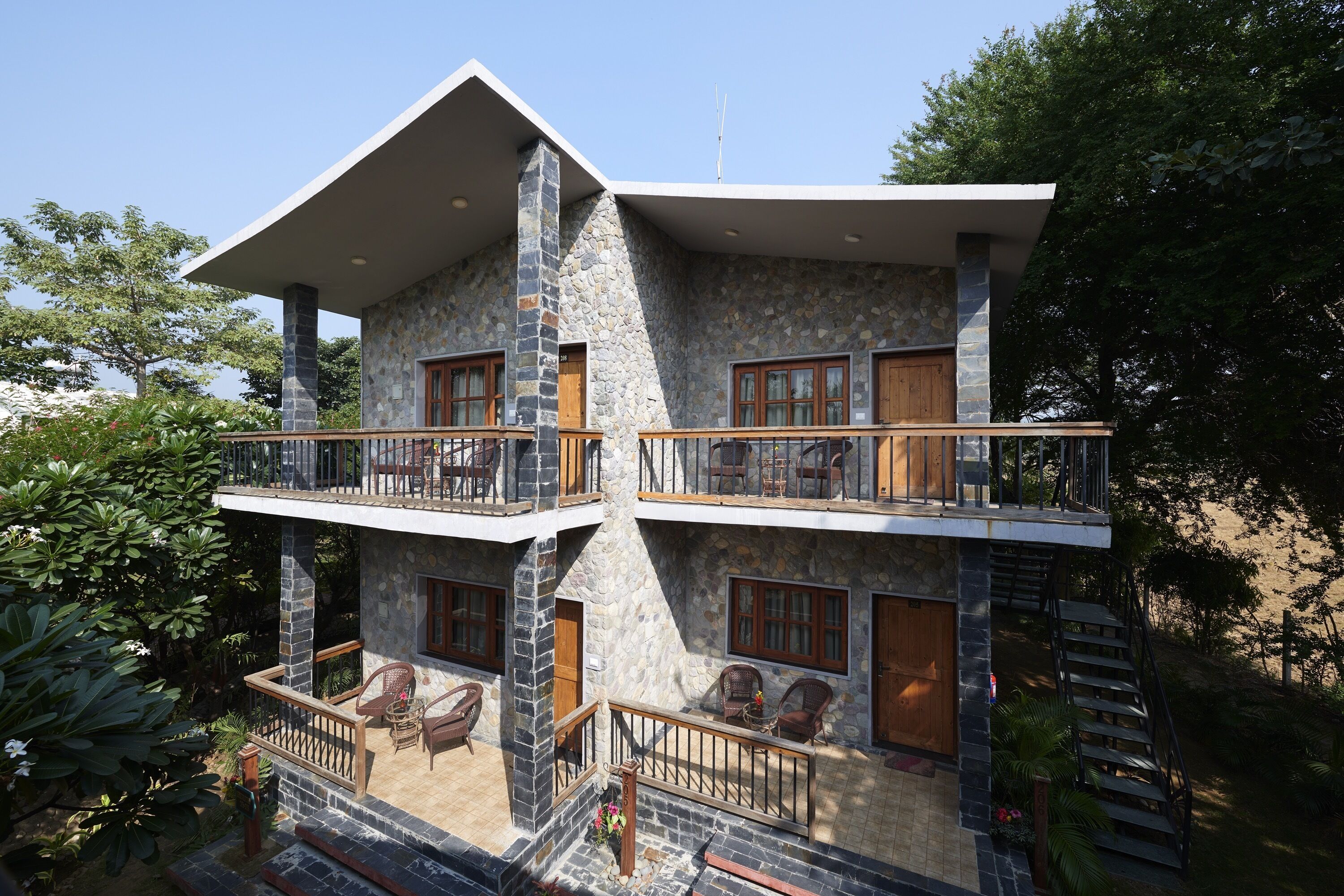 A two-story stone building with balconies, outdoor seating, and a staircase.