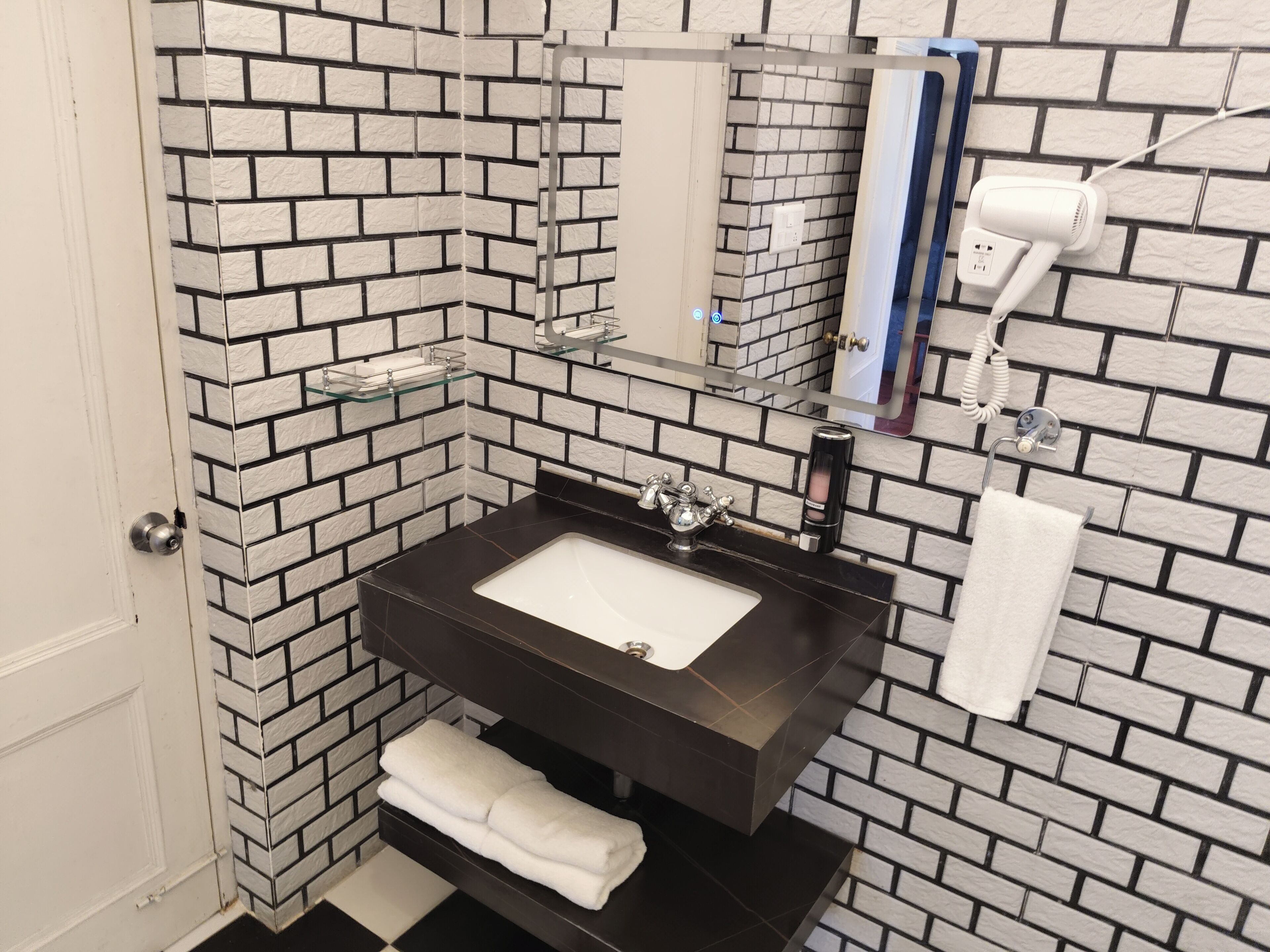 Un baño con un lavabo negro, azulejos blancos, un espejo, un perchero y un secador de pelo.