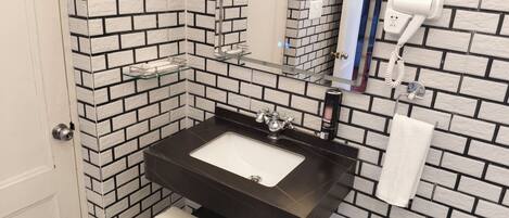 Un baño con un lavabo negro, azulejos blancos, un espejo, un perchero y un secador de pelo.