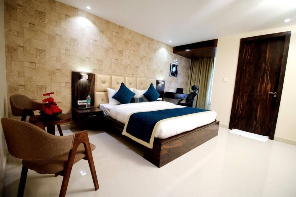 A hotel room with a large bed, a desk, a chair, and a small table with a bottle and red flowers.