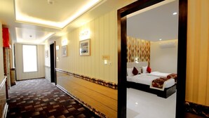 A hotel corridor with a patterned carpet, a wooden floor, a framed picture, and a bed with red pillows. - Pinnacle by Click Hotels, Lucknow (Lucknow)