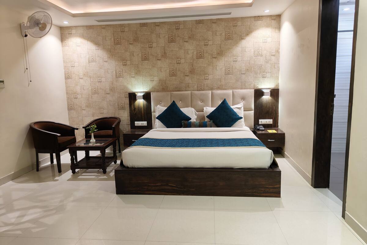 A modern bedroom with a large bed, two bedside tables, a desk, a chair, and a wall-mounted fan.