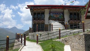 A traditional building with a red roof and decorative windows, situated on a stone staircase with a clear view of the surrounding mountains. - Yangkhil Resort (Trongsa)