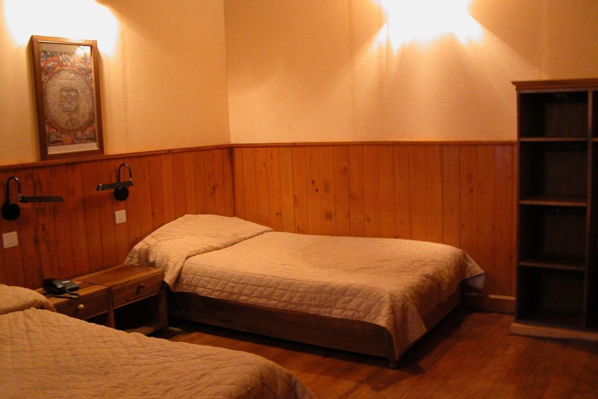 Een kamer met twee bedden, houten wanden, een nachtkastje met een lamp en een lijst met een foto aan de muur.