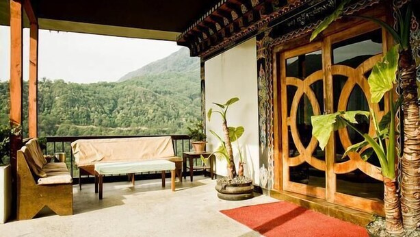 A balcony with a view of a mountainous landscape, a wooden bench, a table, and potted plants. - Yangkhil Resort (Trongsa)