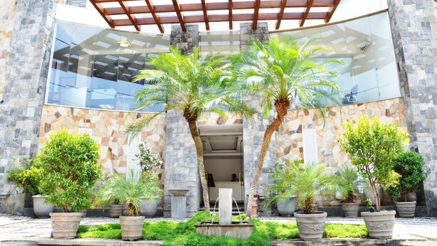 Un bâtiment à la façade en pierre, agrémenté d’une pergola en bois et de plantes en pot devant l’entrée.