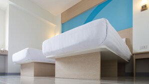 Une chambre d’hôtel moderne avec un grand lit, une petite table de chevet et une lampe fixée au mur.