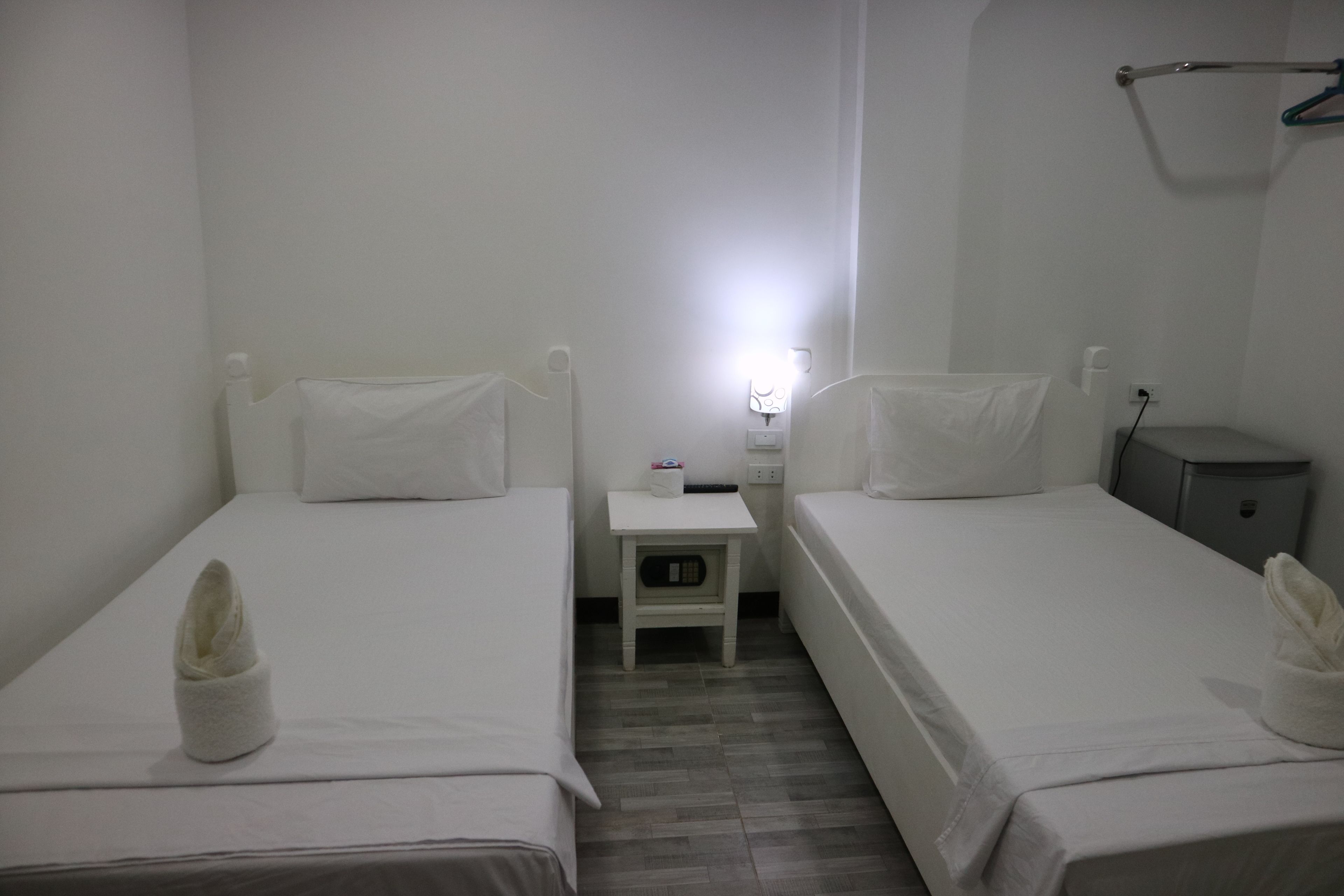 A hotel room with two single beds, a small bedside table with a lamp, a nightstand, and a wardrobe.