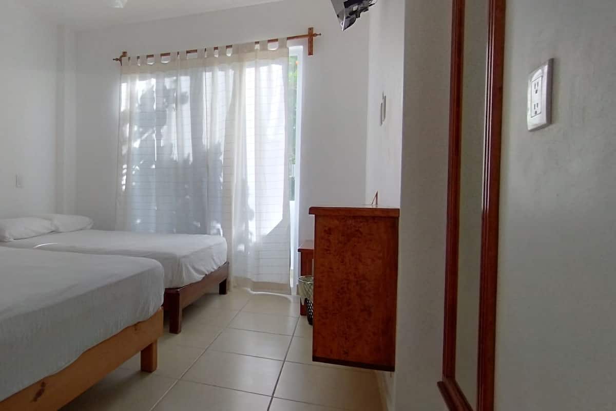 Quarto com duas camas, um armário de madeira e uma janela com cortinas.