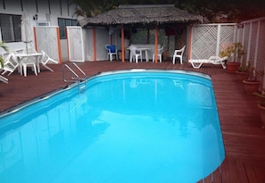 A swimming pool with a wooden deck, white lounge chairs, and a covered seating area. - Aniva's Place (Apia)