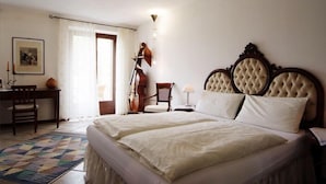 Quarto com uma cama grande, escrivaninha, cadeira, um violino e uma luminária.