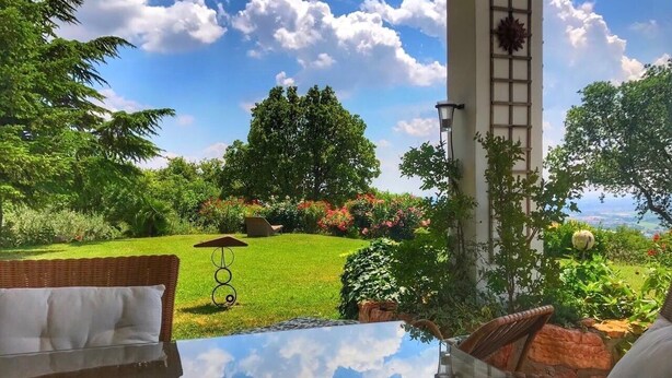 Uma mesa com tampo de vidro e vista para um jardim bem cuidado e um céu limpo.