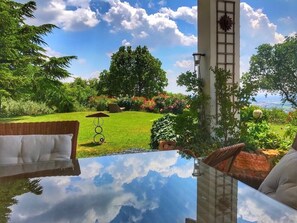 A glass-top table with a view of a well-maintained garden and a clear sky. - Bed and breakfast bei Romy (Verona)