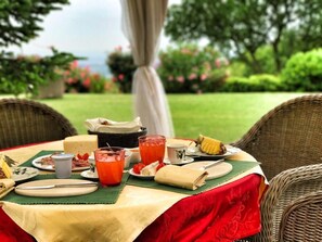 Una mesa al aire libre con diversos alimentos, como queso, frutas y bebidas, cubierta por un mantel verde.