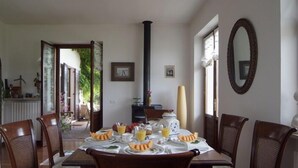 Uma sala de jantar com mesa posta para o café da manhã, cadeiras, uma chaminé alta preta e um espelho na parede.