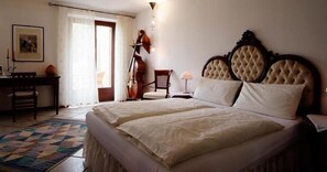 Un dormitorio con una cama grande, un escritorio, una silla, un violonchelo y una lámpara.