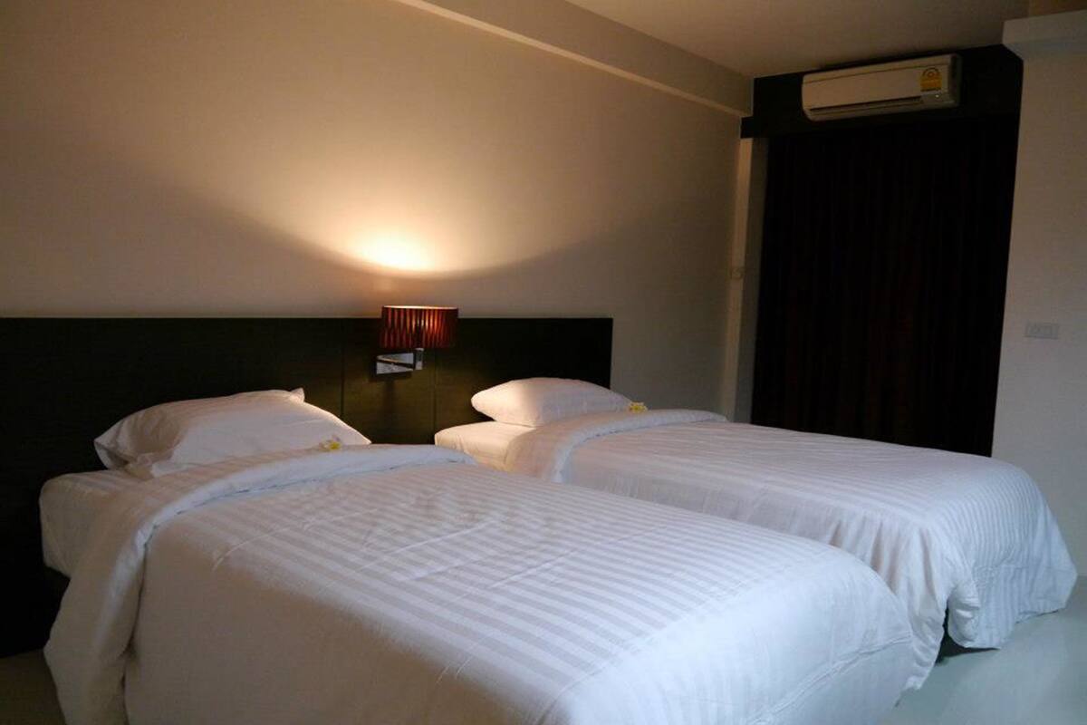 Habitación de hotel con dos camas, aire acondicionado de pared y mesita de noche con lámpara.