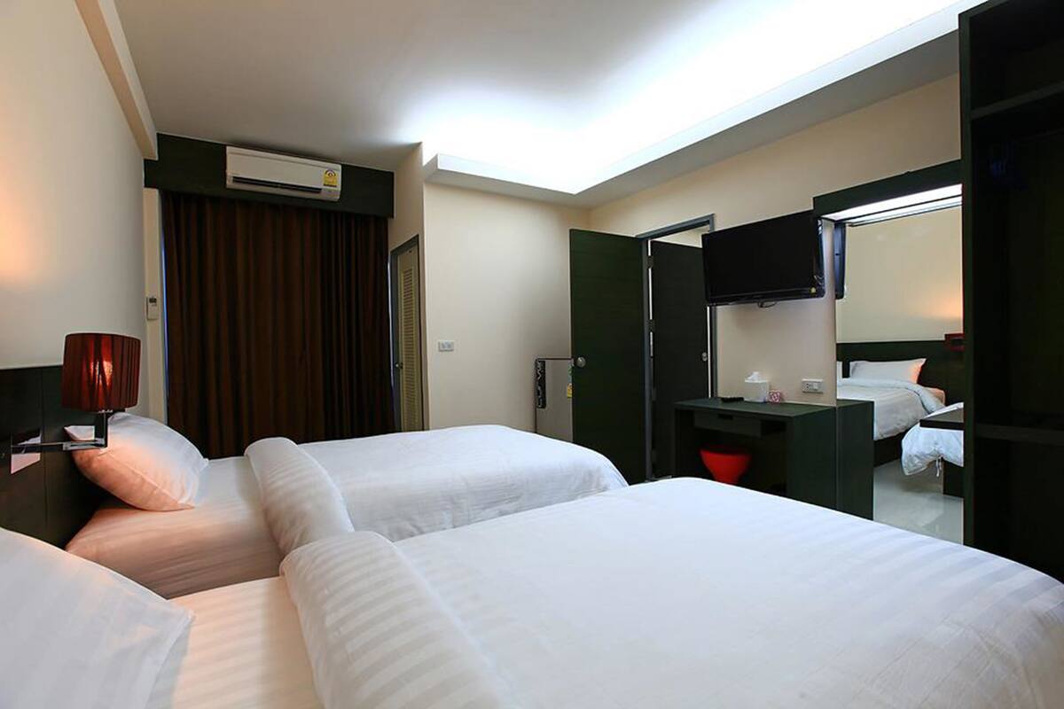 Habitación de hotel con dos camas, un escritorio con silla, un televisor de pantalla plana y un equipo de aire acondicionado.
