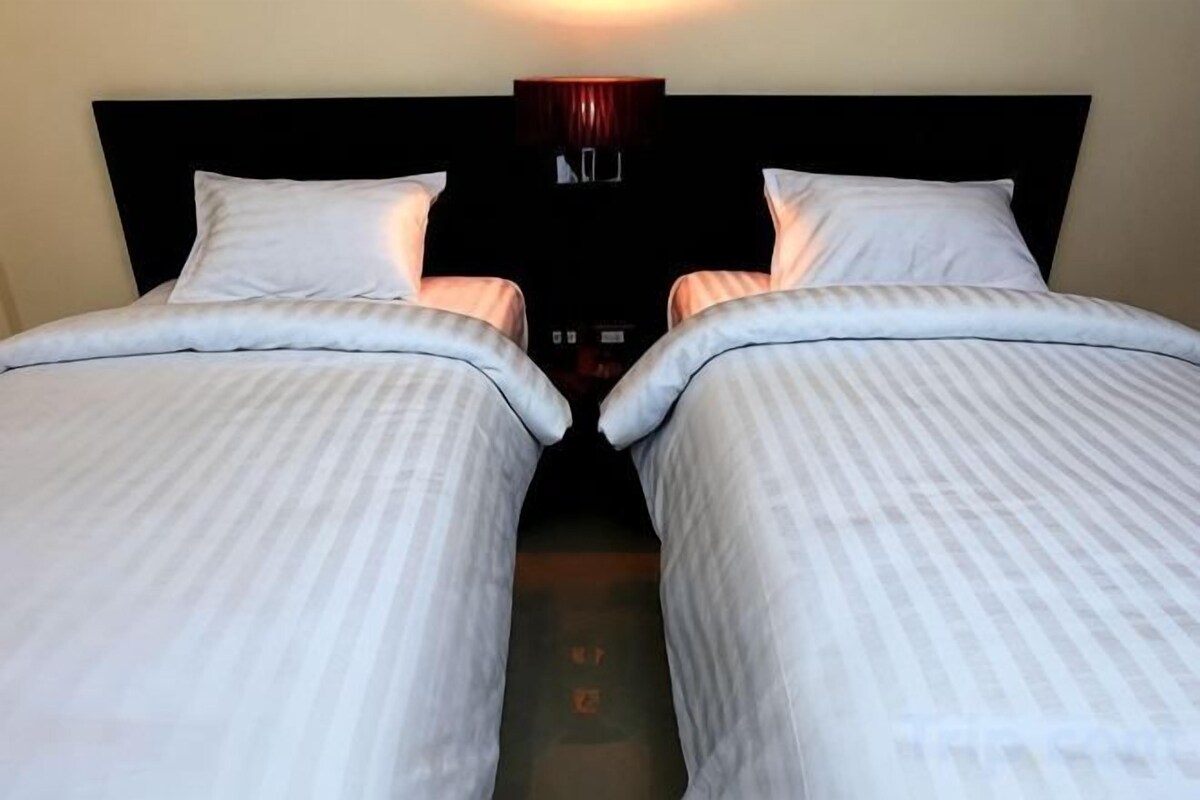 A hotel room with two beds, a dark headboard, and a wall-mounted light fixture.