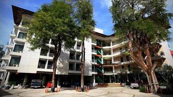 A multi-story building with a courtyard, trees, and a car parked in front.