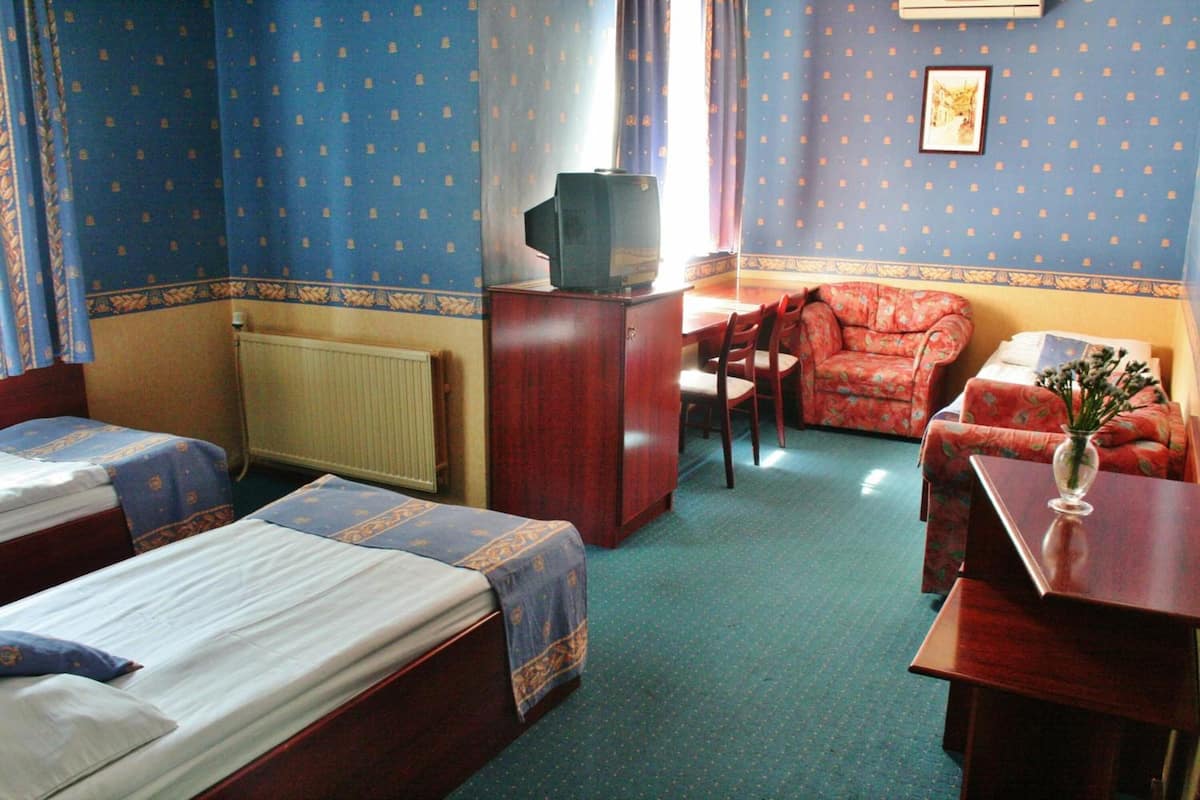 A hotel room with two single beds, a wooden desk, a chair, a sofa, and a television on a cabinet.