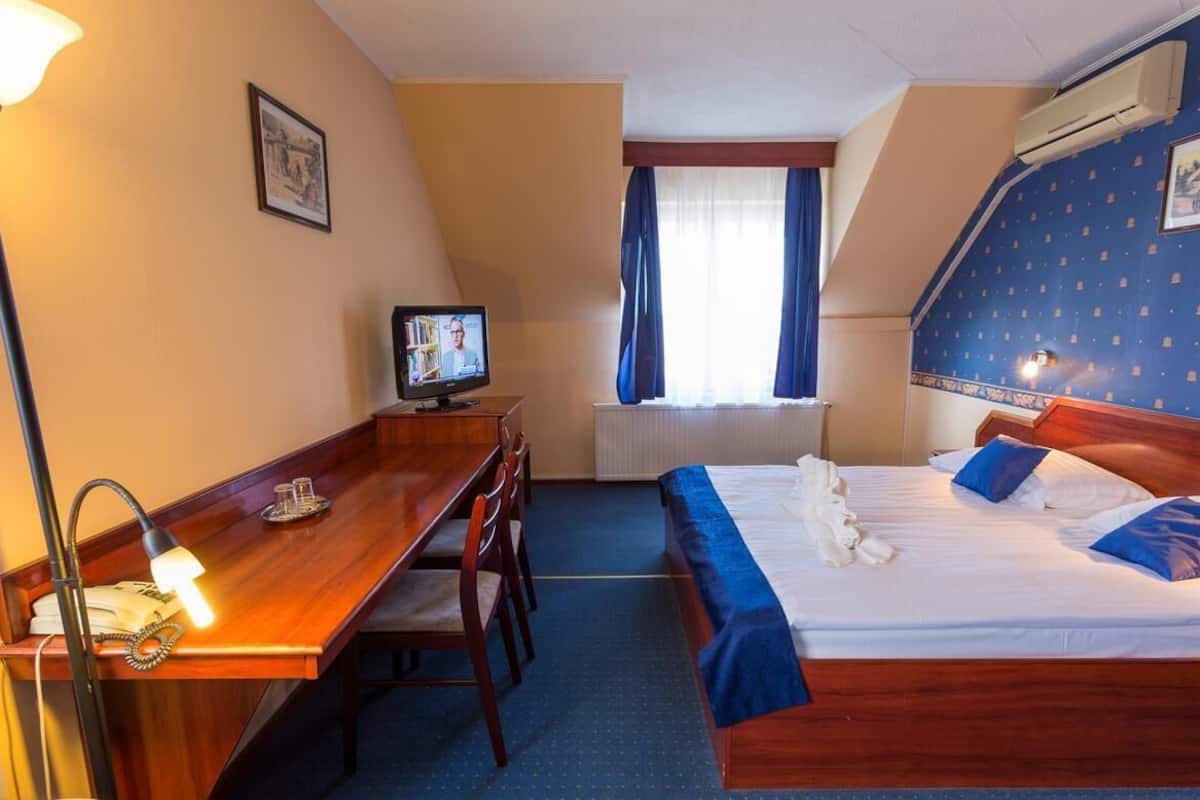 A hotel room with a wooden desk, a bed with blue bedding, and a television on the desk.