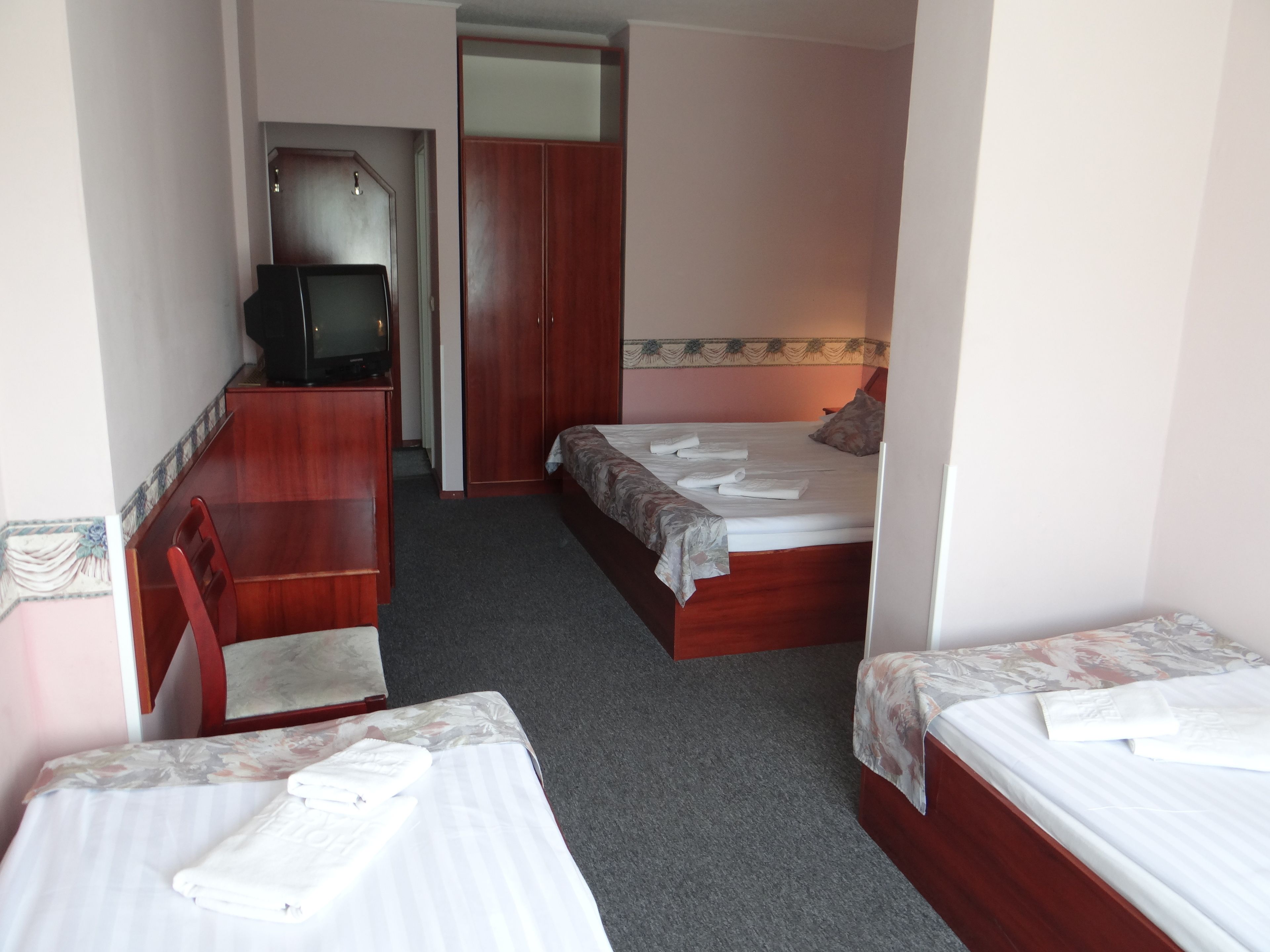 Ett hotellrum med två separata sängar, ett skrivbord i trä med en tv och en garderob.