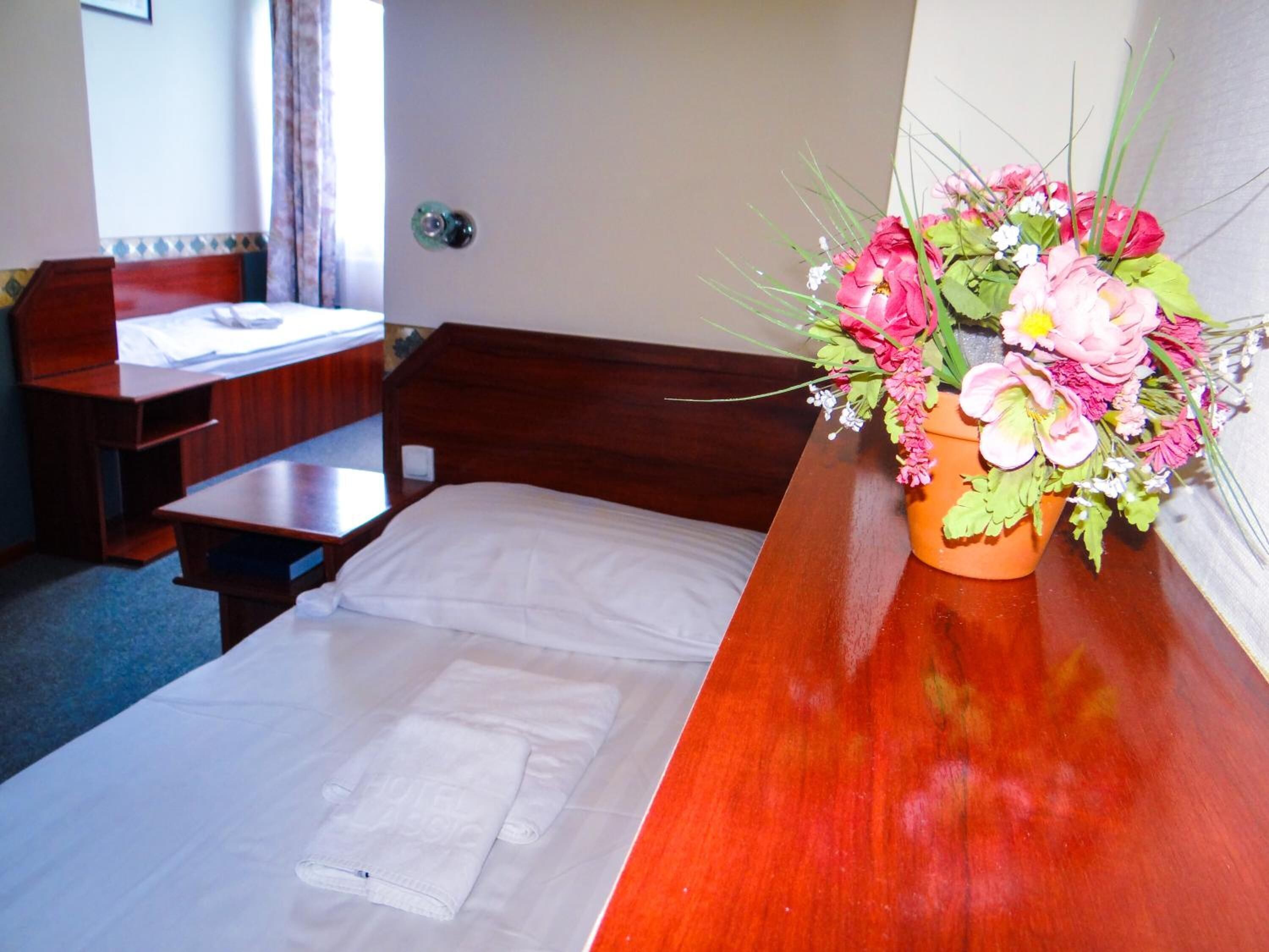 A hotel room with a wooden bed, a wooden nightstand, a desk, and a window with curtains.