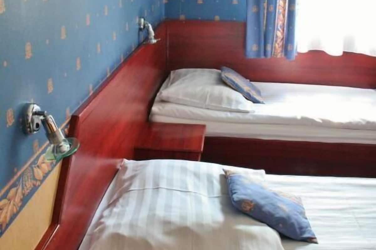 A room with two wooden beds, a small table, and a window with curtains.