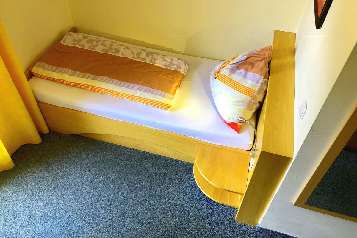 Une petite chambre avec un lit simple, un cadre en bois, un matelas et un oreiller.