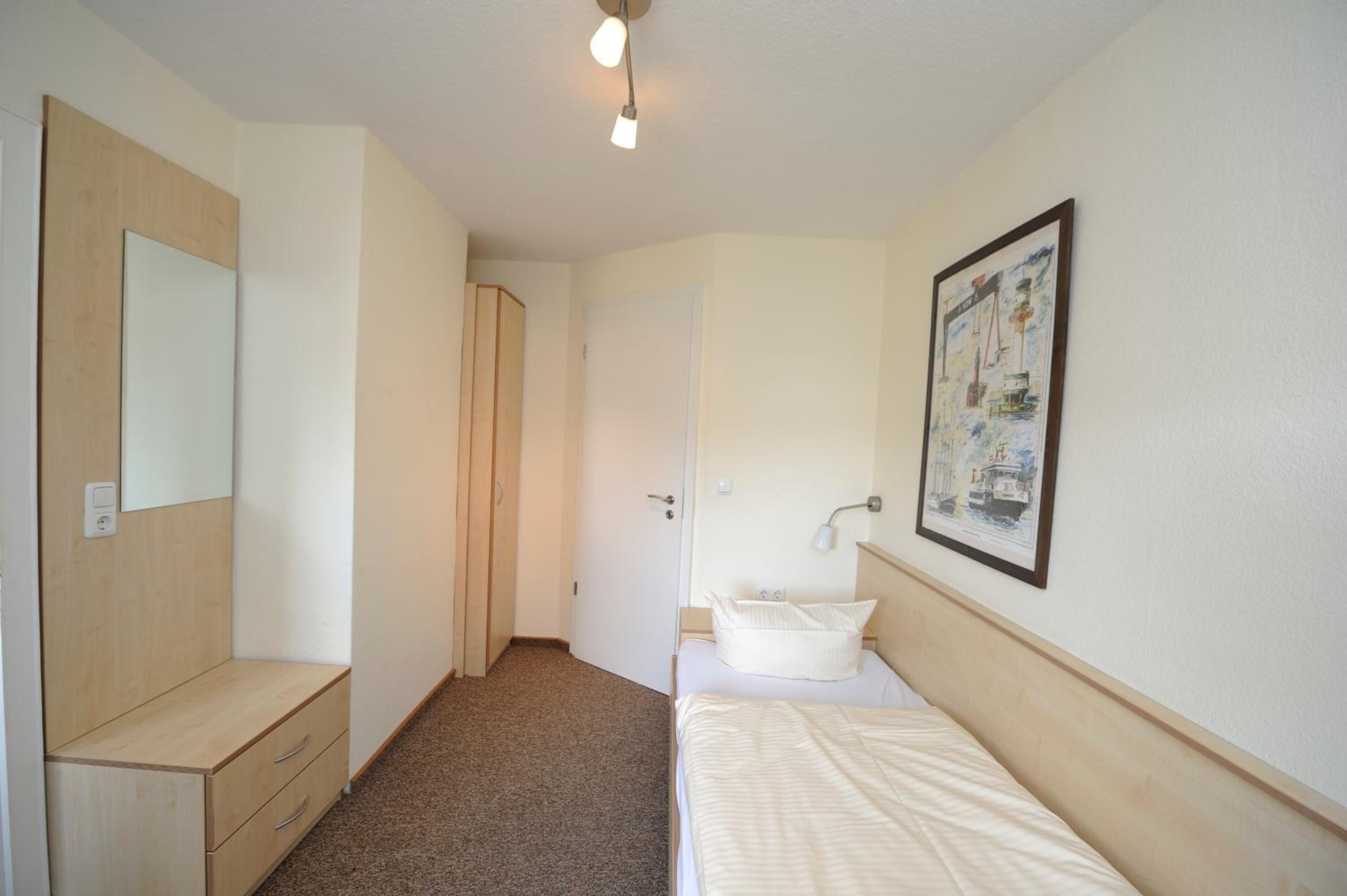 Un dormitorio con cama, mesita de noche, espejo, armario y baño con lavabo y un cuadro en la pared.