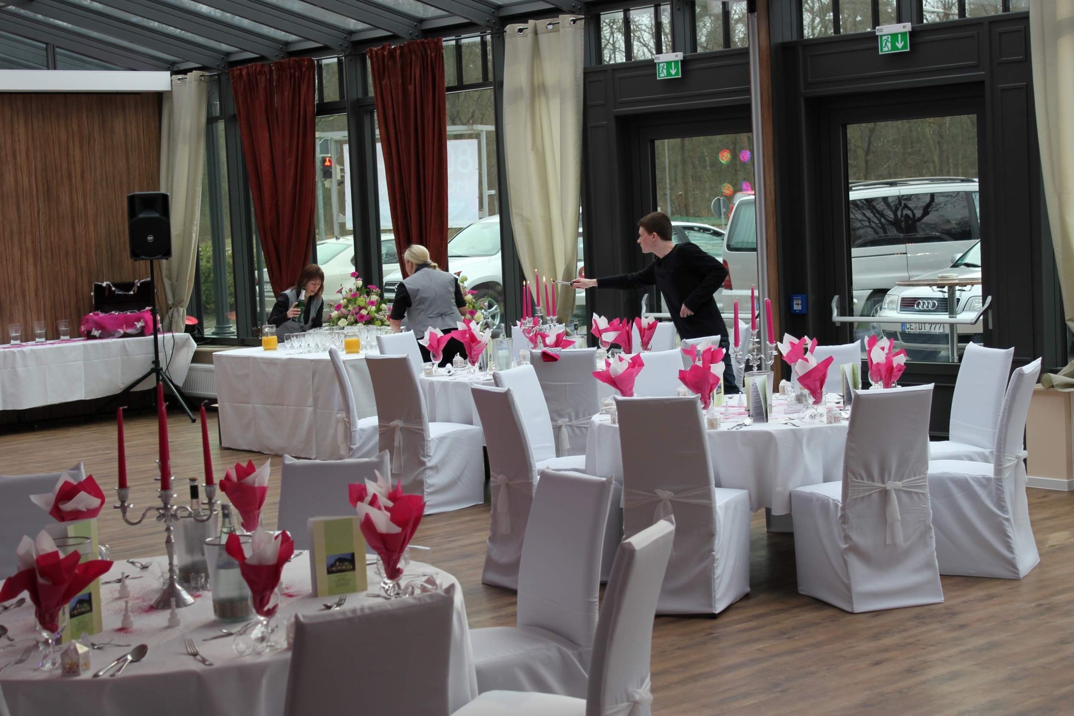 Une salle de banquet avec des tables rondes dressées pour un événement formel, agrémentées de nappes blanches et de centres de table floraux roses.