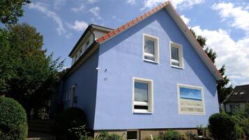 Uma casa de dois andares com fachada azul, número 31, com um pequeno jardim frontal e uma chaminé visível.