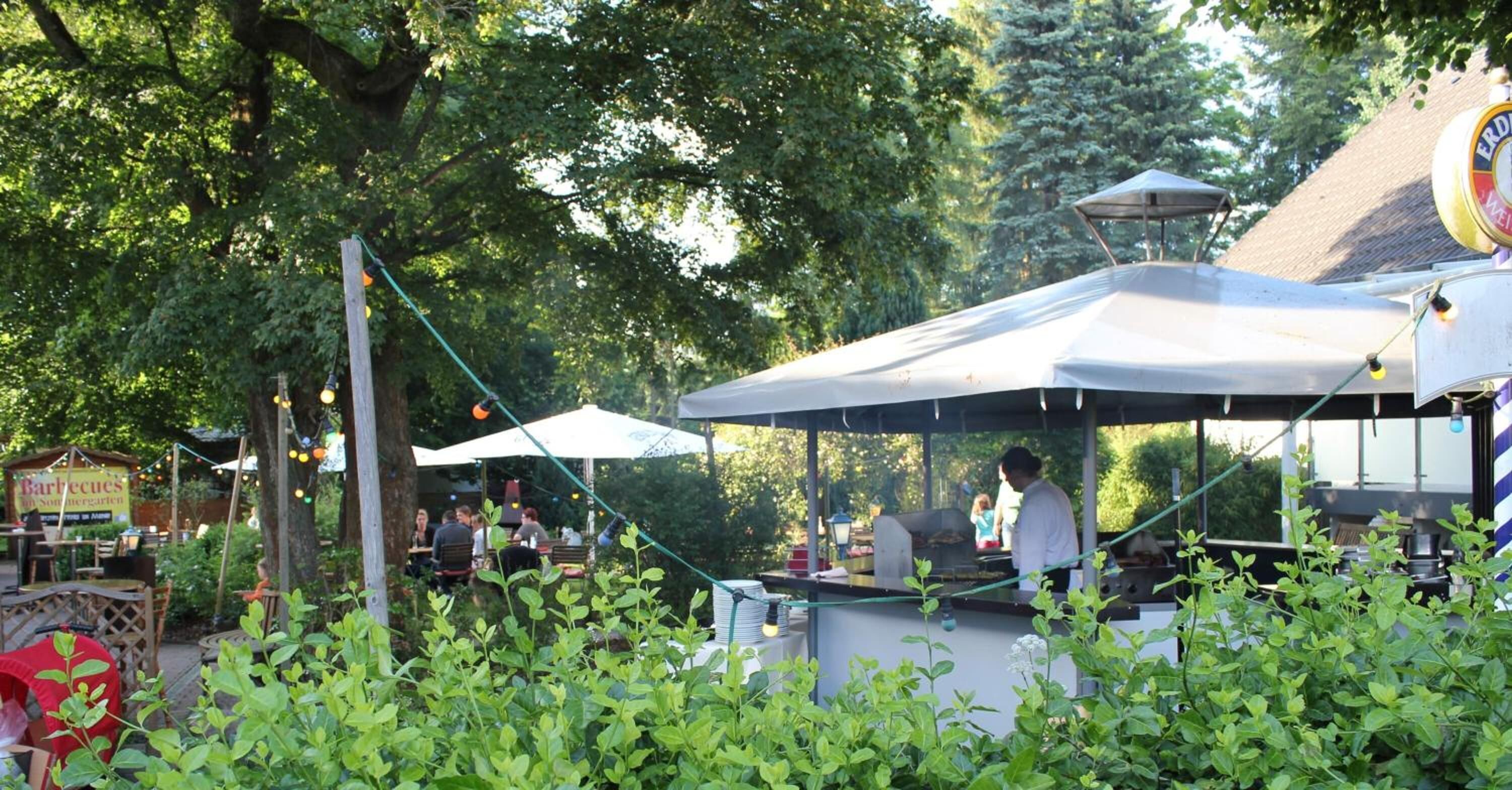 An outdoor dining area with tables and umbrellas, surrounded by greenery.