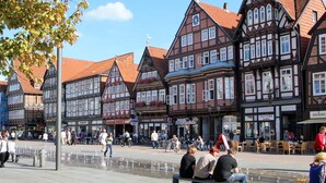 Una plaza tradicional europea con edificios históricos de entramado de madera, mesas al aire libre y una zona peatonal.