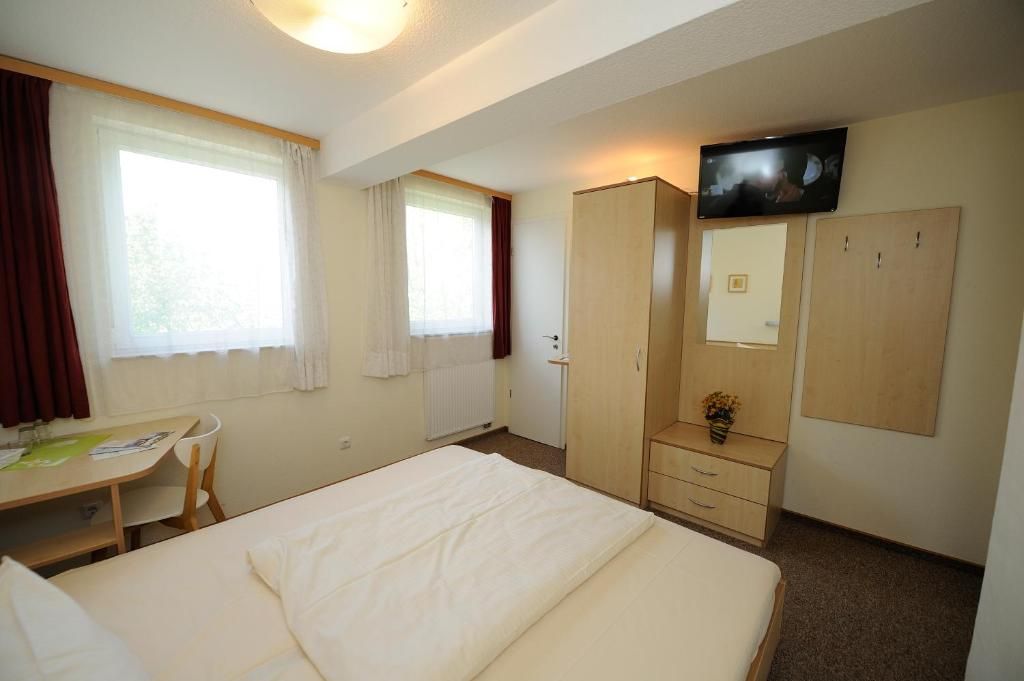 A hotel room with a bed, a desk, a chair, a wardrobe, a television, and a window with curtains.