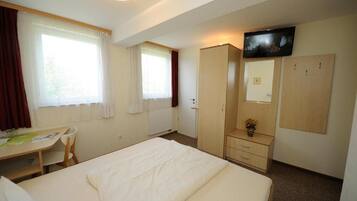 A hotel room with a bed, a desk, a chair, a wardrobe, a television, and a window with curtains.