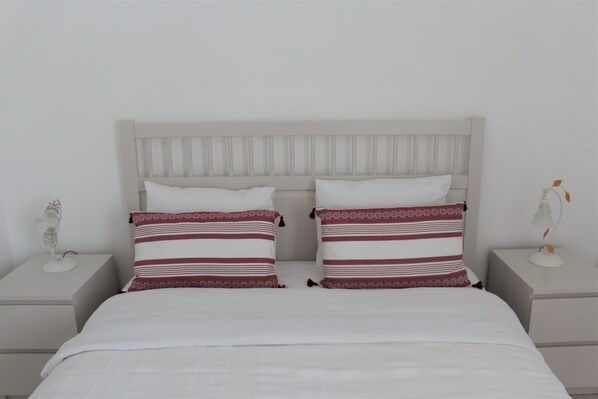 A bed with a white headboard, two pillows with red and white stripes, and a white bedspread.